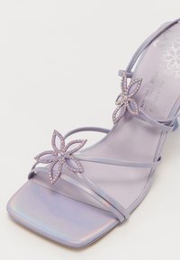 Sandale vegan lilas à brides avec un bout carré, dotée de deux accents floraux ornés de strass et d'une finition irisée.
