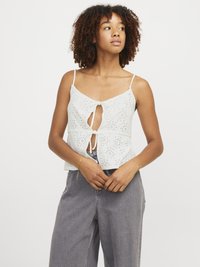 Hvit bomull crop top med nøkkelhull foran og knyting, med lufthuller og tynne stropper, kombinert med grå vide bukser.