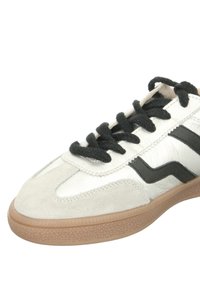 Zapatilla blanca y negra con una parte superior de ante y cuero, con cordones negros y suela de goma, mostrando un diseño de zigzag en los lados.