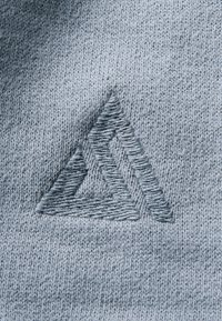Motif géométrique triangulaire en relief tricoté dans un tissu gris clair, montrant une texture détaillée et des variations de points.