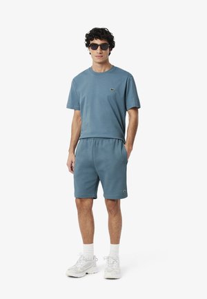 Ensemble en coton bleu comprenant un t-shirt et un short avec une taille élastique, des manches courtes, et un petit logo sur la poitrine. Associé à des baskets blanches.