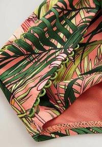 Tissu à imprimé floral mettant en avant des feuilles vertes sur un fond rose, avec des bordures en accent vert et des détails de couture texturés le long des bords.