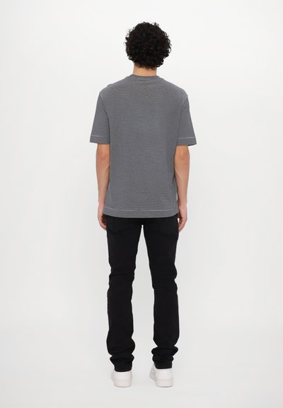 T-shirt cinza riscada com mangas curtas, corte relaxado e bainha arredondada, combinada com jeans pretos e ténis brancos.