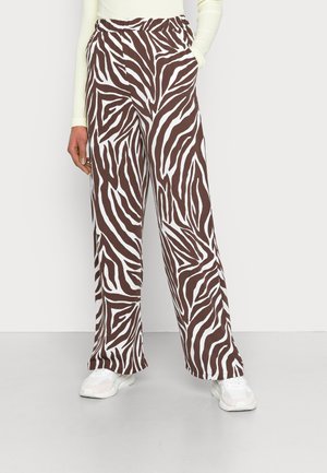 Calças largas com padrão de zebra castanho e branco, com cintura elástica e bolsos laterais, combinadas com ténis brancos sobre um fundo claro.