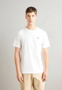 Hvid kortærmet T-shirt i bomuld med rund halsudskæring og et lille sort logo på venstre side af brystet. Casual pasform, glat tekstur.