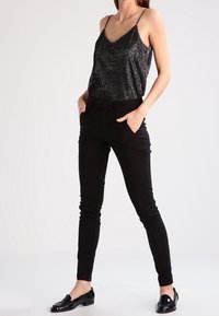 Pantalons noirs ajustés associés à un débardeur métallique noir à fines bretelles. La tenue comprend des mocassins noirs et présente un design épuré.