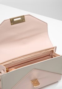 Borsa strutturata di un rosa chiaro con esterno testurizzato, hardware dorato e un'ampia apertura che rivela un interno foderato e una tasca con zip.