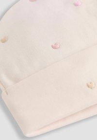 Un bonnet pour bébé rose doux, fabriqué en coton, avec des petits cœurs brodés en rose et beige. Bord replié avec une texture lisse.