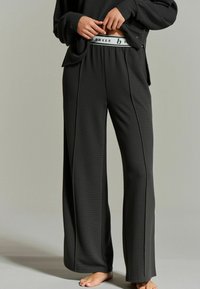 Wijduitlopende zwarte sweatpants gemaakt van textuurstof, met een contrasterende witte tailleband met "BAKER" opdruk en zijnaad.