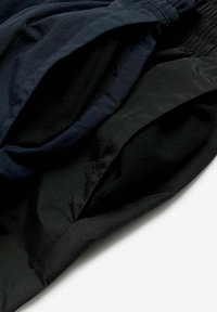 Tengerészkék és fekete rövidnadrág, texturált belső béléssel. Rugalmas derékrésszel és kontrasztos anyagrétegekkel rendelkezik, sima külső kialakítással.