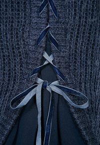 Close-up van een marineblauwe gebreide stof met een fluwelen lint dat is doorgestoken en in een strik is geknoopt over een donkere blauwe stof eronder.