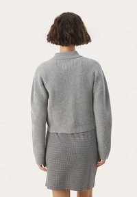 Sivý rebrovaný pletený sveter s vysokým golierom a padnutými ramenami, nosený cez sukňu s čierno-bielym vzorom houndstooth.