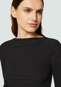 Robe noire texturée avec un col bateau, présentant un design froissé. Gros plan sur le tissu et les détails du corsage.