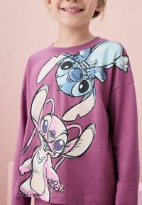 Lila sweatshirt med tecknade figurer; mjukt material, lång ärm, stor grafisk design fram med blå och rosa figurer.