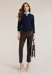 Granatowy dzianinowy kardigan z talią typu peplum, nałożony na jasnoniebieską koszulę w paski. Brązowe spodnie z eko skóry i cieliste szpilki dopełniają stylizację.