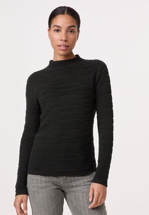 Schwarzer, strukturierter Pullover mit hohem Ausschnitt und langen Ärmeln. Hat ein geripptes Design mit dezenten horizontalen Linien. Kombiniert mit grauen verzierten Jeans.