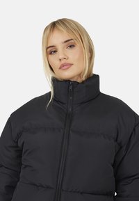 Giacca a vento nera con colletto alto, chiusura con zip e motivo trapuntato. Caratterizzata da una texture liscia e una vestibilità leggermente oversize.