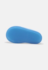 Blue rubber shoe sole with textured, wavy pattern. Slightly rounded shape with a flat edge and embossed logo near the center.