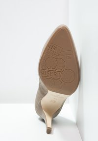 Beige suede pointed-toe high heel shoe shown from sole view with embossed decorative coin patterns and slim heel.
