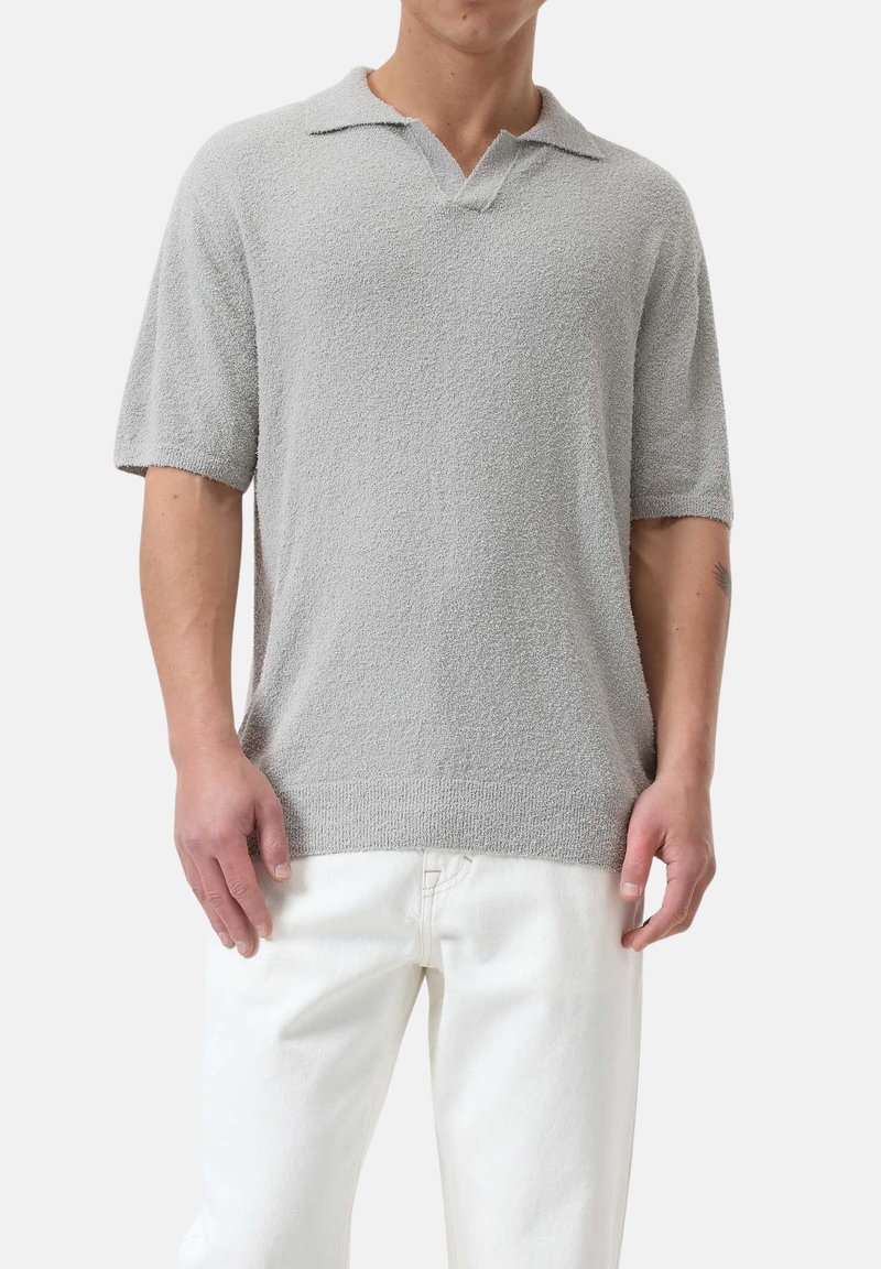 Polo grigio a maniche corte con un tessuto testurizzato, design a V, polsini e orlo a coste, abbinato a pantaloni bianchi.