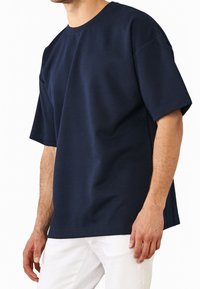 Camiseta de manga corta en azul marino con escote redondo, hecha de una tela suave y texturizada; cuenta con un corte holgado y hombros caídos.