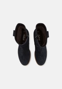 Bottines en daim bleu foncé avec une texture lisse, fermeture à glissière latérale et petite boucle pour un enfilage facile. Semelles en caoutchouc beige pour une bonne adhérence.