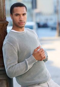 Grau gesc hl itzter Pullover mit gerippter Textur, der einen weißen Kragen und gestreifte Bündchen aufweist. Der Stoff wirkt weich und leicht.