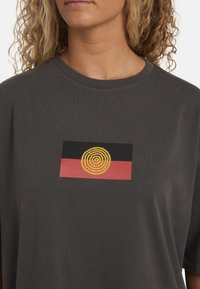 Donkergrijze katoenen T-shirt met korte mouwen en een gedrukt cirkelpatroon in geel, zwart en rood in het midden.