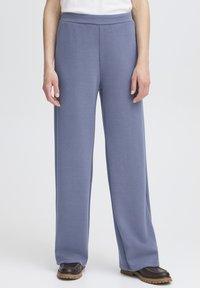 Pantalons larges bleu clair en tissu doux et texturé avec une taille haute élastique, associés à des chaussures marron à semelles épaisses.