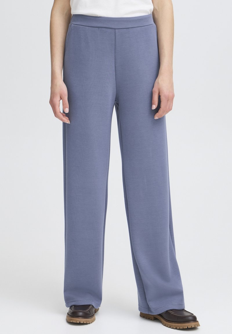 Pantalons larges bleu clair en tissu doux et texturé avec une taille haute élastique, associés à des chaussures marron à semelles épaisses.