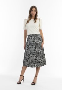 Cremefarvet ribbet top med korte puffærmer, parret med en mid-længde sort og hvid leopardprint nederdel. Modellen har sorte strop sandaler på.