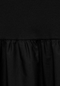 Robe noire avec un corsage en tricot ajusté et une jupe en tissu doux et froncé. Texture lisse tout au long, avec une couleur et un design cohérents.