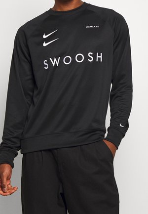 Zwart shirt met lange mouwen met witte Nike swoosh-logo's op borst en mouw, "SWOOSH" tekst aan de voorkant en Romeinse cijfers MCMLXXII vlak bij de kraag.