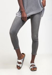 Harmaa neulottu yläosa, istuvat harmaat denim-caprihousut ja hopeanväriset liukusandaalit mustilla ja ruskeilla pohjilla. Yksinkertainen muotoilu, säädettävillä remmeillä.