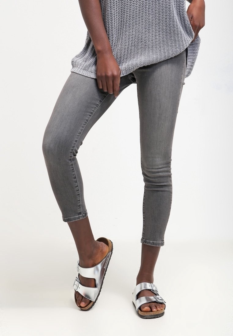 Harmaa neulottu yläosa, istuvat harmaat denim-caprihousut ja hopeanväriset liukusandaalit mustilla ja ruskeilla pohjilla. Yksinkertainen muotoilu, säädettävillä remmeillä.