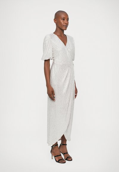 Fénylő ezüst színű ruhához hasonló wrap dress, rövid puffujjú, textúrált anyagból készült, oldalsó hasítékkal, fekete, pántos magassarkú szandálokkal párosítva.