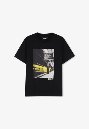 T-shirt noir DKNY avec un graphique jaune et noir d’un quai de métro et un train en mouvement, avec un panneau New York Stories.