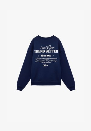 Granatowy sweter wykonany z mieszanki bawełny, z białym napisem "Jestem Teraz TRENDY WSKAZUJĄCY Od 1994" oraz dodatkowymi elementami dekoracyjnymi i okrągłym dekoltem.