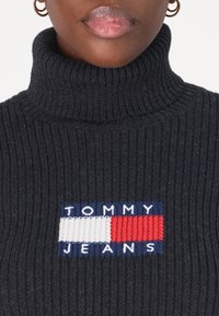 Maglione girocollo nero a coste con un logo ricamato rettangolare composto da sezioni rosse, bianche e blu con la scritta "TOMMY JEANS."