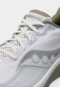 Λευκό και γκρι αθλητικό παπούτσι Saucony με λευκά κορδόνια πάνω σε διάτρητο πλέγμα και λογότυπο στην πλαϊνή επιφάνεια.