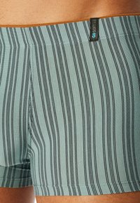 Striped men's underwear in a light teal color with black vertical stripes. Features a contrasting waistband and soft, stretchy fabric.