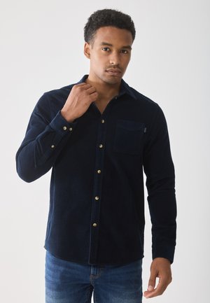 Navy corduroy button-up shirt with a chest pocket, gold buttons, and long sleeves. Fabric has a textured finish and a straight hem.