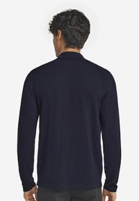 Mörkblå långärmad polo-shirt med en slät textur, en klassisk krage och figursydda manschetter, visad bakifrån.