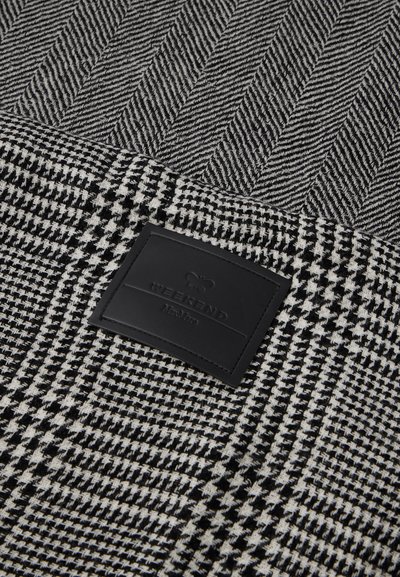 Szőtt fekete-fehér szövet, amelyen houndstooth és herringbone minták láthatók, egy téglalap alakú fekete bőr címkével, amelyen a "WEEKEND" felirat szerepel.