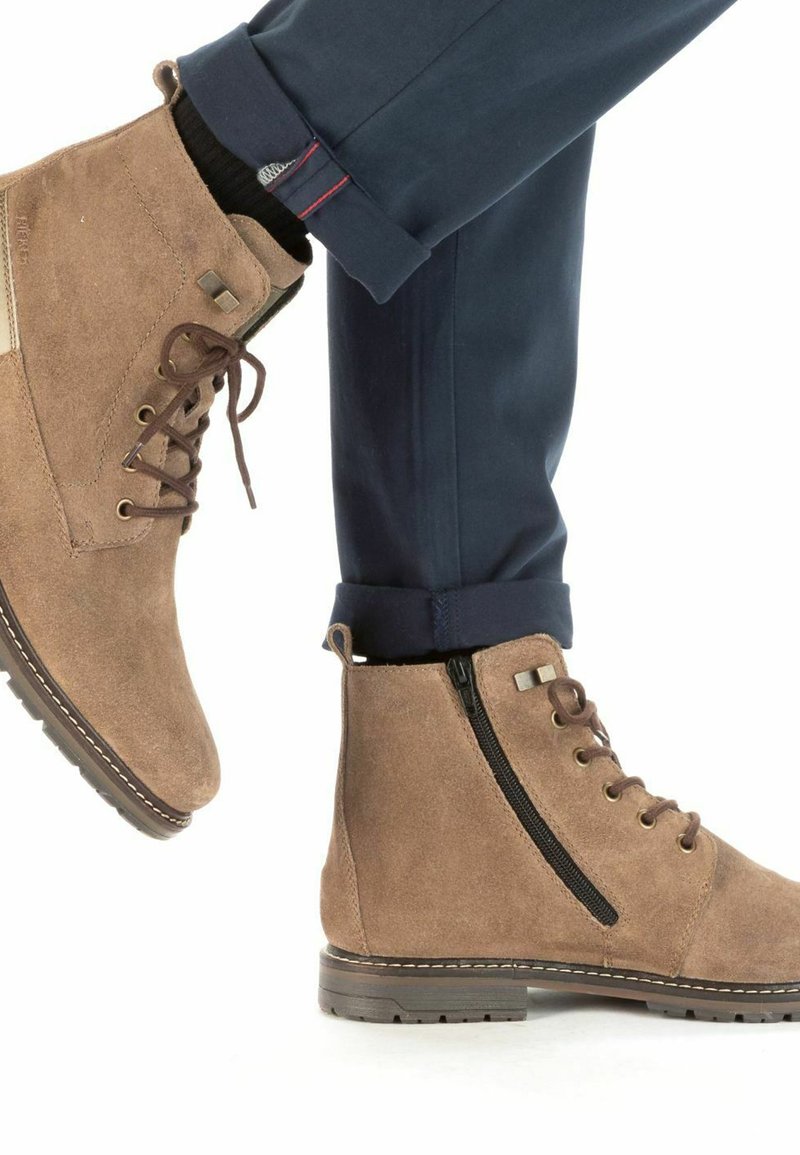 Stivali alla caviglia in suede marrone con lacci e chiusura con cerniera, superficie texturizzata e suole in gomma, abbinati a pantaloni blu navy.