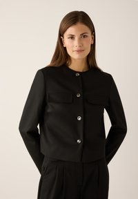 Black cropped jacket featuring shiny silver buttons, two front pockets, round neckline, and smooth fabric texture.