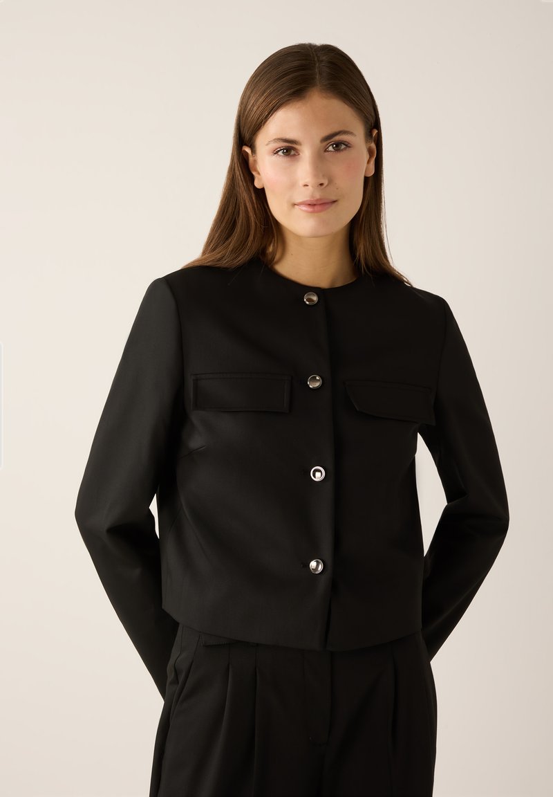 Black cropped jacket featuring shiny silver buttons, two front pockets, round neckline, and smooth fabric texture.