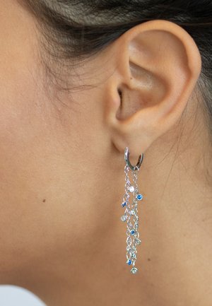 Silberne Creolen mit herabhängenden Ketten, die mit blauen und klaren Edelsteinen verziert sind, präsentieren ein filigranes Design und unterschiedliche Texturen.