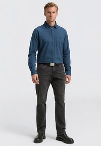 Blå langærmet skjorte med knapper og brystlomme, kombineret med mørkegrå jeans og sorte ankelstøvler med en sølvfarvet bæltespænde.