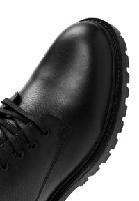 Botines negros de cuero con textura suave, punta redonda, ojales metálicos y suela rugosa con diseño antideslizante para una mejor tracción.